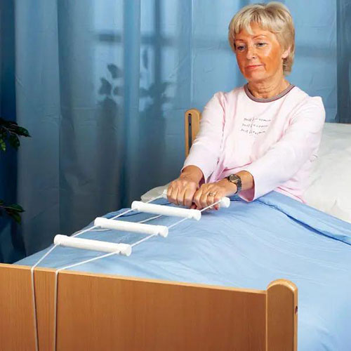 Eine weiße Bettleiter die an einem Krankenbett angebracht ist und an der sich eine ältere Dame hochzieht.jpg